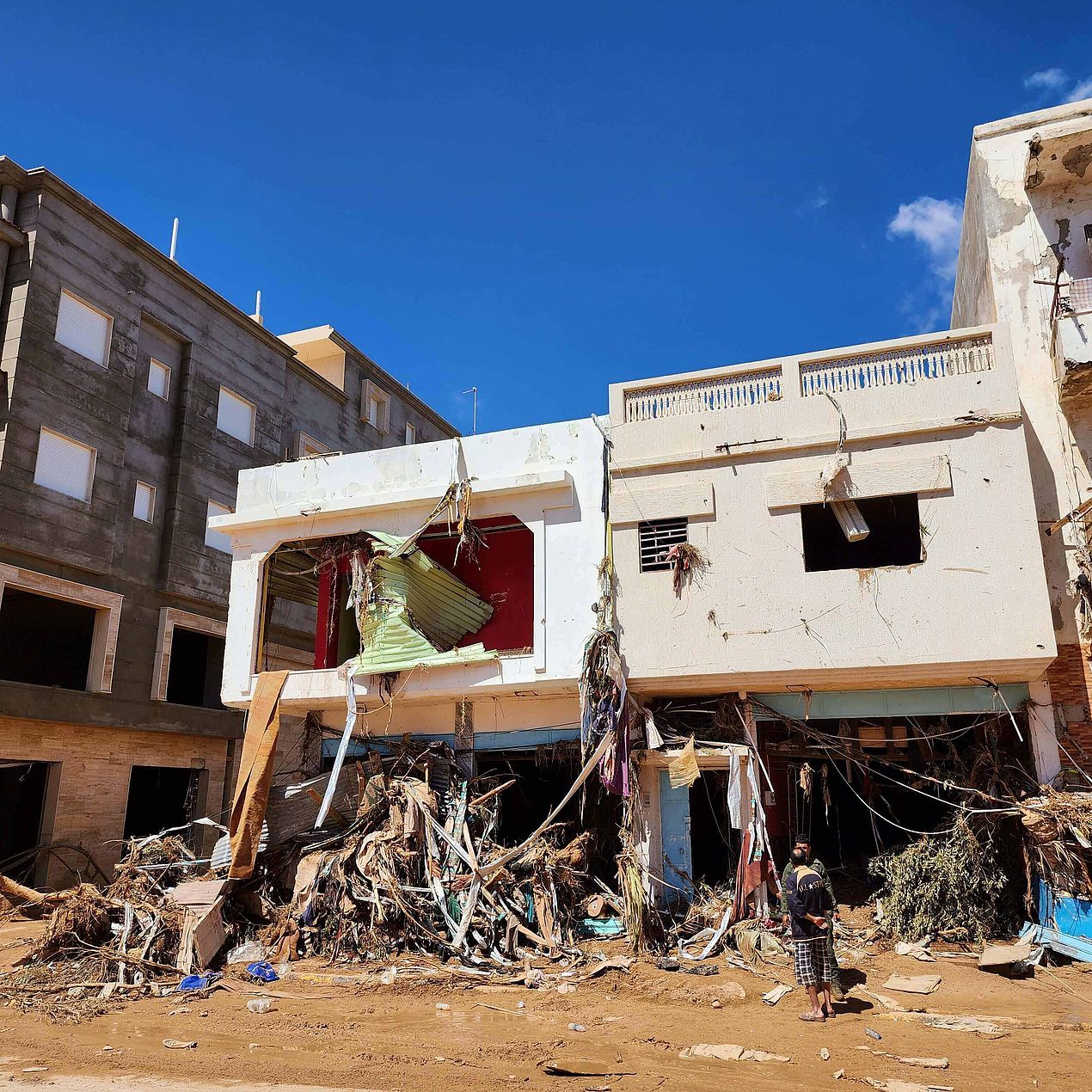 Männer vor zerstörten Häusern Zwei Männer stehen vor stark verwüsteten Häusern nach den verheerenden Überschwemmungen in Libyen.