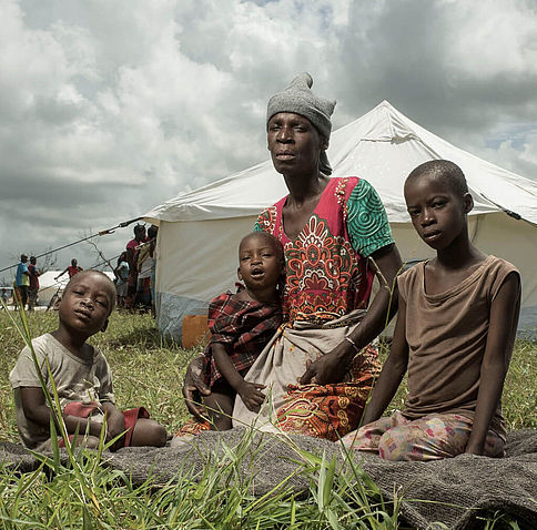 Isabel und ihre Enkelkinder sitzen vor ihrem neuen Zuhause: einem Zelt auf einem ehemaligen Fußballfeld.