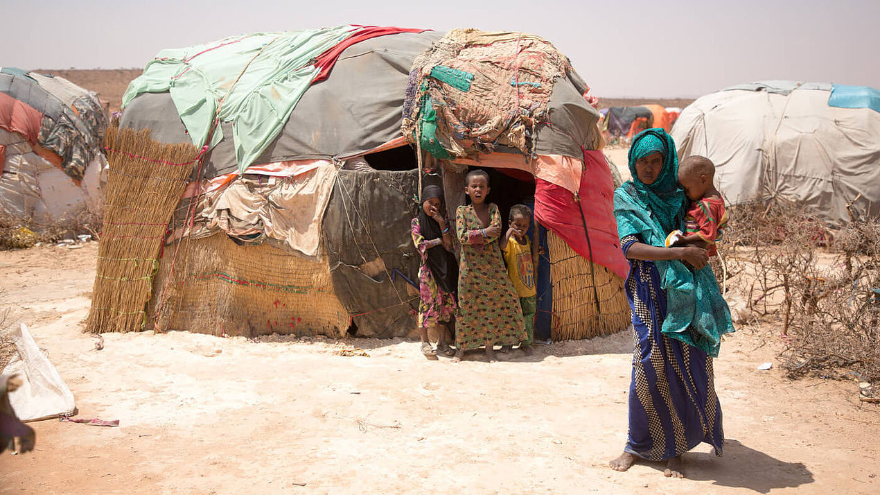 Eine Frau hält ihr Kind auf dem Arm, im Hintergrund stehen drei weitere Kinder vor dem Eingang ihres Zeltes im Flüchtlingscamp Burao in Somalia