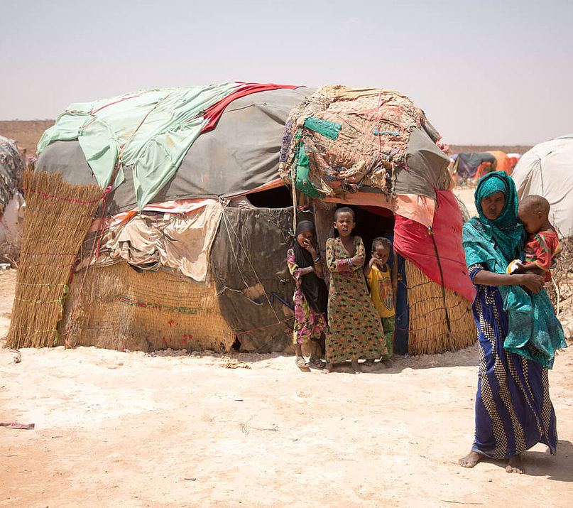 Eine Frau hält ihr Kind auf dem Arm, im Hintergrund stehen drei weitere Kinder vor dem Eingang ihres Zeltes im Flüchtlingscamp Burao in Somalia
