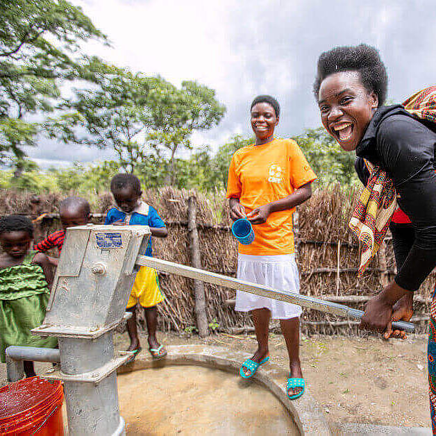 Eine lachende Frau pumpt Wasser über eine von CARE gebaute Wasserpumpe.