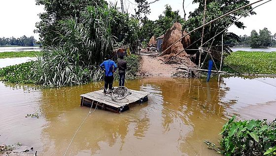 Zwei Männer stehen auf einem Floß und überqueren ein überschwemmtes gebiet in Bangladesch
