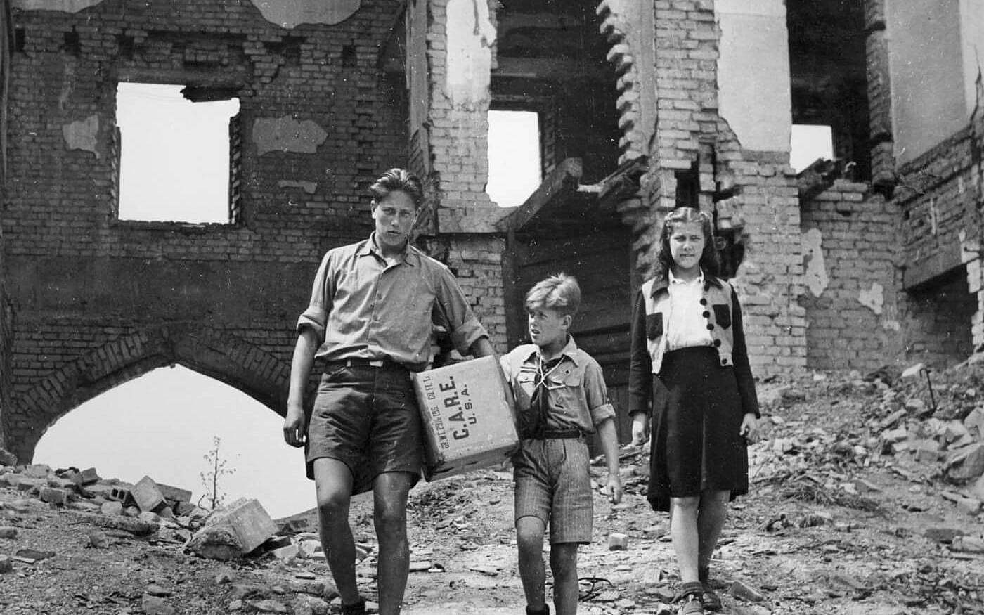 Ein Mann und zwei Kinder tragen ein CARE-Paket.