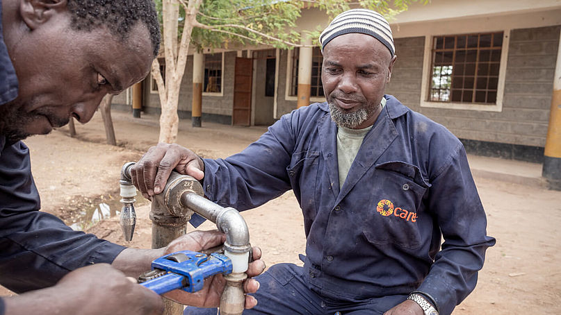 Zwei Männer im Blaumann reparieren einen Wasserhahn im Flüchtlingscamp Dadaab in Kenia.
