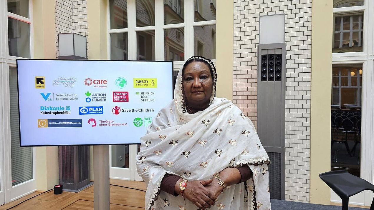 Fatima vor einem Bildschirm mit Logos Fatima steht vor einem Bildschirm mit Logos von Hilfsorganisationen.