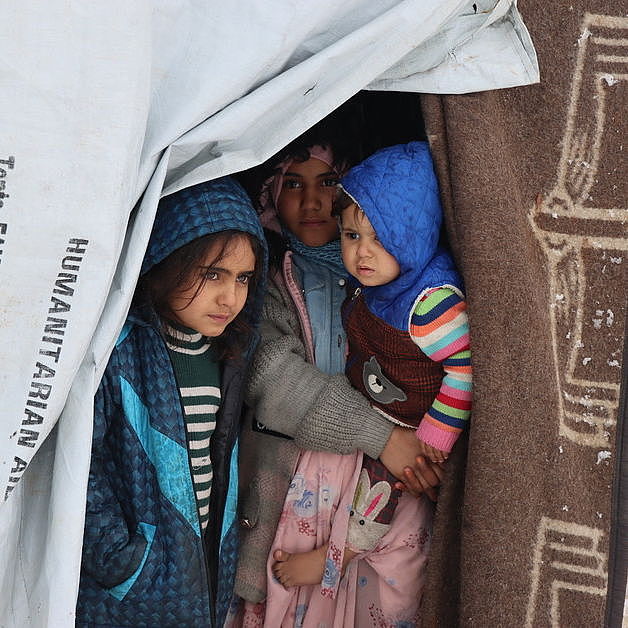 Drei syrische Kinder stehen in einem Zelt