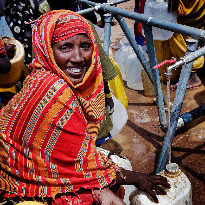 Eine lächelnde Frau im roten Gewand zapft Wasser in einen Kanister