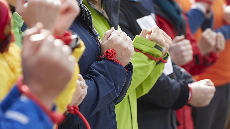 Ein rotes Seil bindet die Hände von mehreren Menschen zusammen.