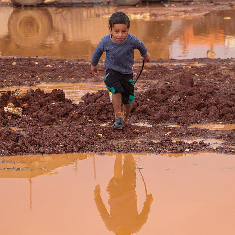 Ein Junge in einem Flüchtlingscamp in Syrien läuft durch Matsch.