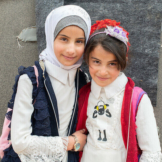 Zwei syrische Maedchen stehen in einem Camp für Gefluechtete nebeneinander.