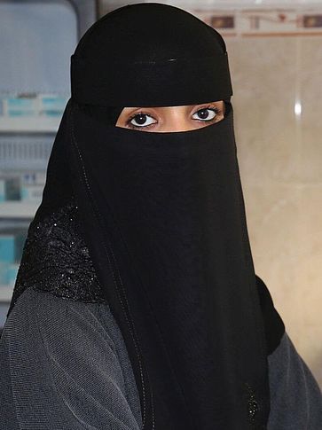 Heba aus dem Jemen schaut in die Kamera, vor ihr steht ein Mikroskop.