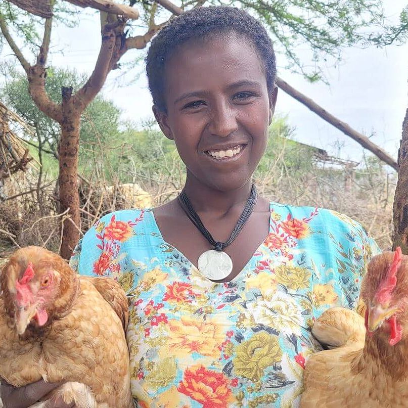 Frau steht draußen und hält zwei Hühner in ihren Armen