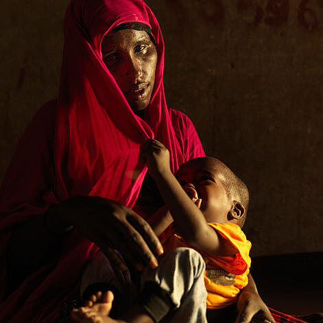 Nasteexos aus Somalia im roten Gewand mit ihrem jüngsten Kind auf dem Schoß