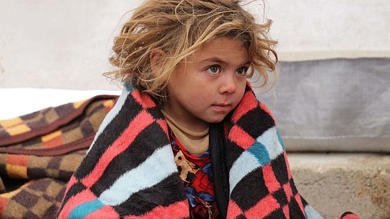 Syrisches Kind sitzt eingehüllt in eine Decke in einem Zelt.