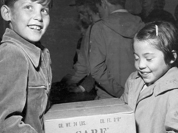 Historisches Foto zweier Kinder, die ein CARE-Paket tragen.