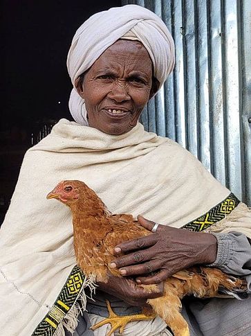 Frau vor einer Hütte mit einem Huhn im Arm