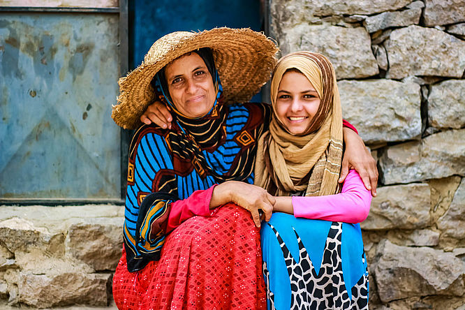 Jemen: Mutter und Tochter sitzen nebeneinander, sie lächeln und haben die Arme umeinander gelegt.