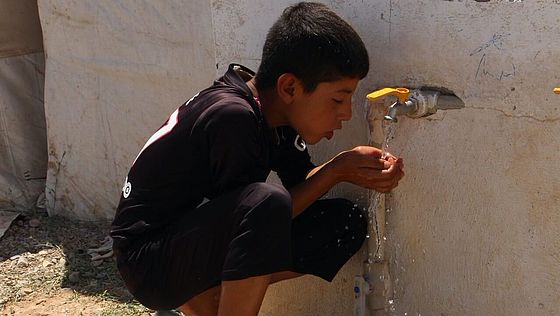 Ein Junge im Irak trinkt aus einem Wasserhahn.