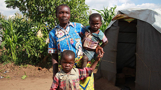 Mutter aus der DR Kongo steht mit zwei kleinen Kindern neben einem Zelt