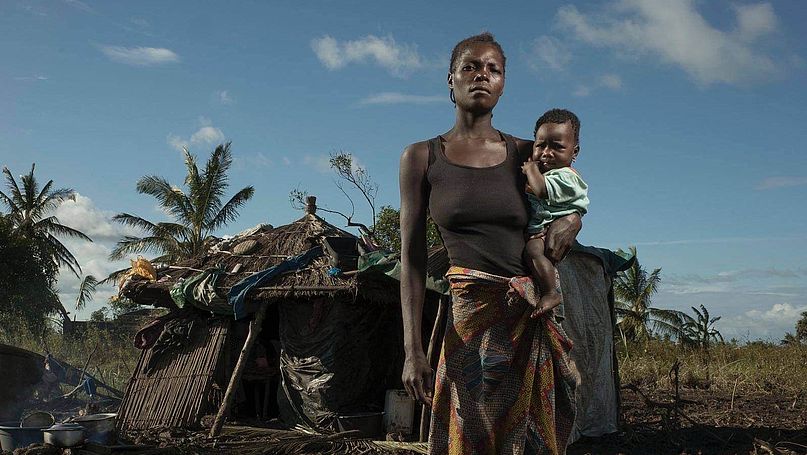 Eine Frau steht mit einem Baby auf dem Arm vor einer durch Zyklon Idai zerstörten Hütte