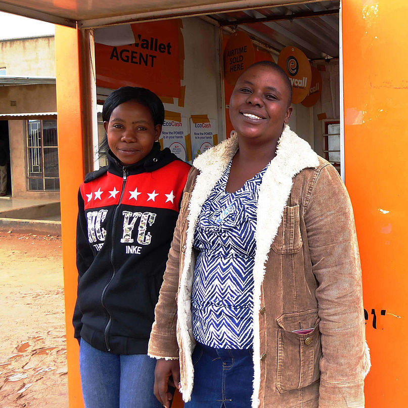 Zwei Frauen stehen vor einem orangen Häuschen und lächeln