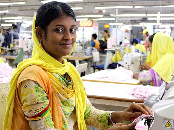 Eine Frau in gelber Kleidung arbeitet in einer Textilfabrik in Bangladesch und lächelt
