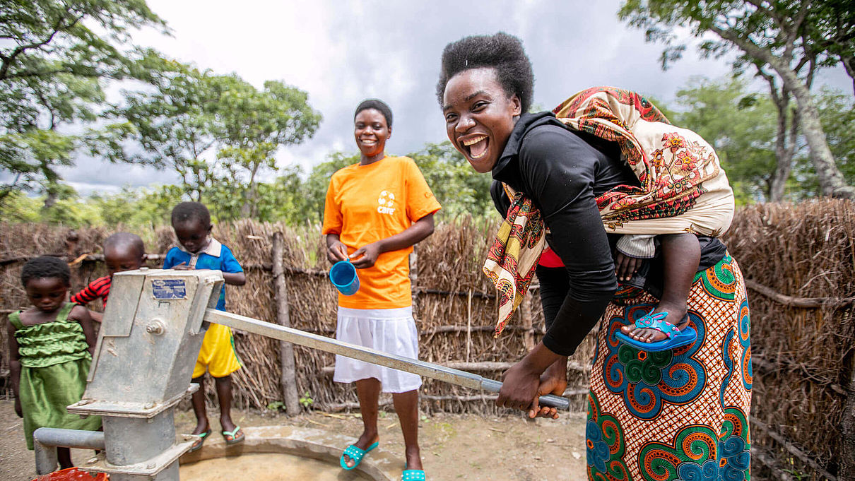 Eine Frau in Sambia pumpt Wasser und lacht in die Kamera