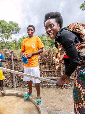 Eine Frau in Sambia pumpt Wasser und lacht in die Kamera