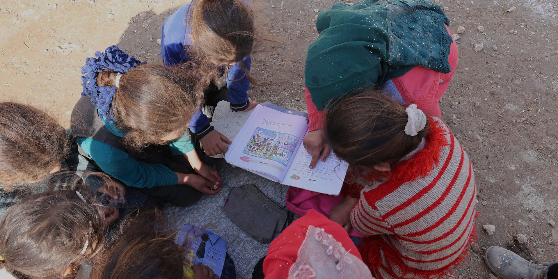 Amra sitzt mit Freundinnen im Kreis und zeigt ihnen etwas in einem Buch.