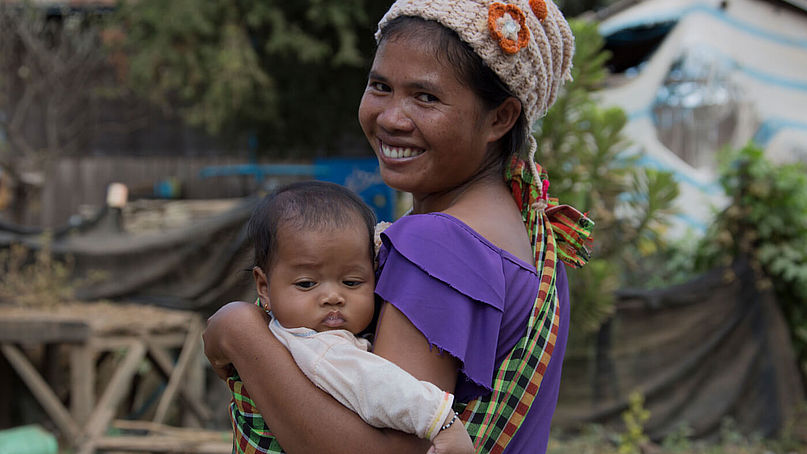 Frau aus Kambodscha lächelt mit ihrer kleinen Tochter auf dem Arm.