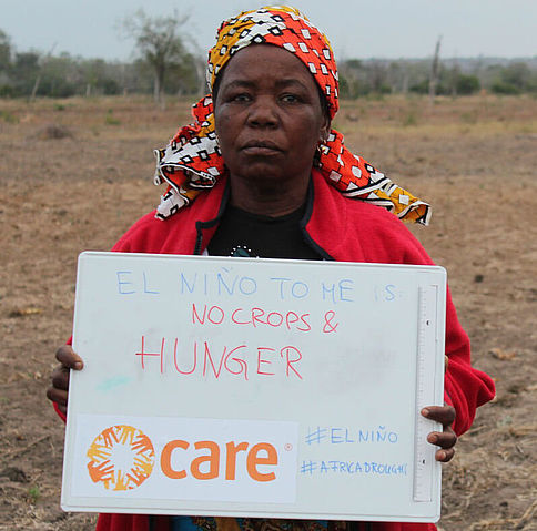 Eine Frau steht auf einem Feld und zeigt ein Schild auf dem steht: El Niño for me is no crops and hunger (El Niño bedeutet für mich keine Ernte und Hunger)