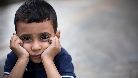 Ein kleiner Junge stützt seinen Kopf in die Hände und guckt traurig
