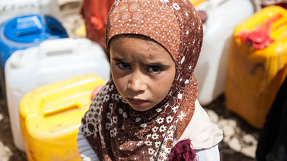 Ein Mädchen im Jemen steht vor großen Wasserkanistern.