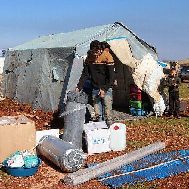 Helfer:innen tragen nach den Erdbeben in Syrien Hilfsgueter in ein Zelt, das einer betroffenen Familie als Notunterkunft dient.