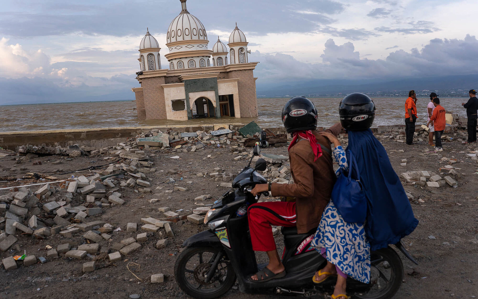 Ein Mann und eine Frau auf einem Motorroller blicken auf eine Moschee, die 2018 vom Tsunami in Indonesien beschädigt wurde.