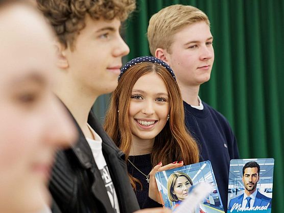 Eine Schuelerin haelt eine Spielkarte des Planspiels in die Kamera