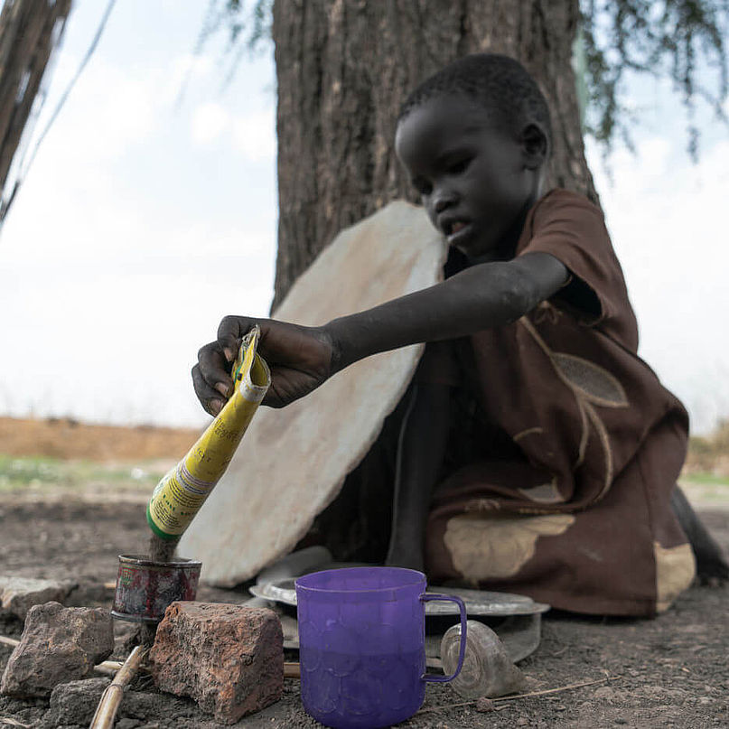 Die fünfjährige Nyahok sitzt unter einem Baum und spielt Kochen.