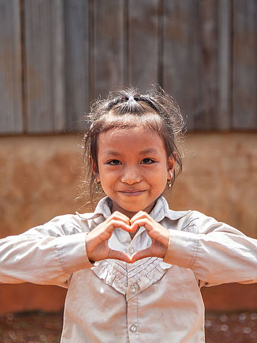 Ein Schulmädchen lächeln in die Kamera und zeigt mit ihren Händen ein Herz