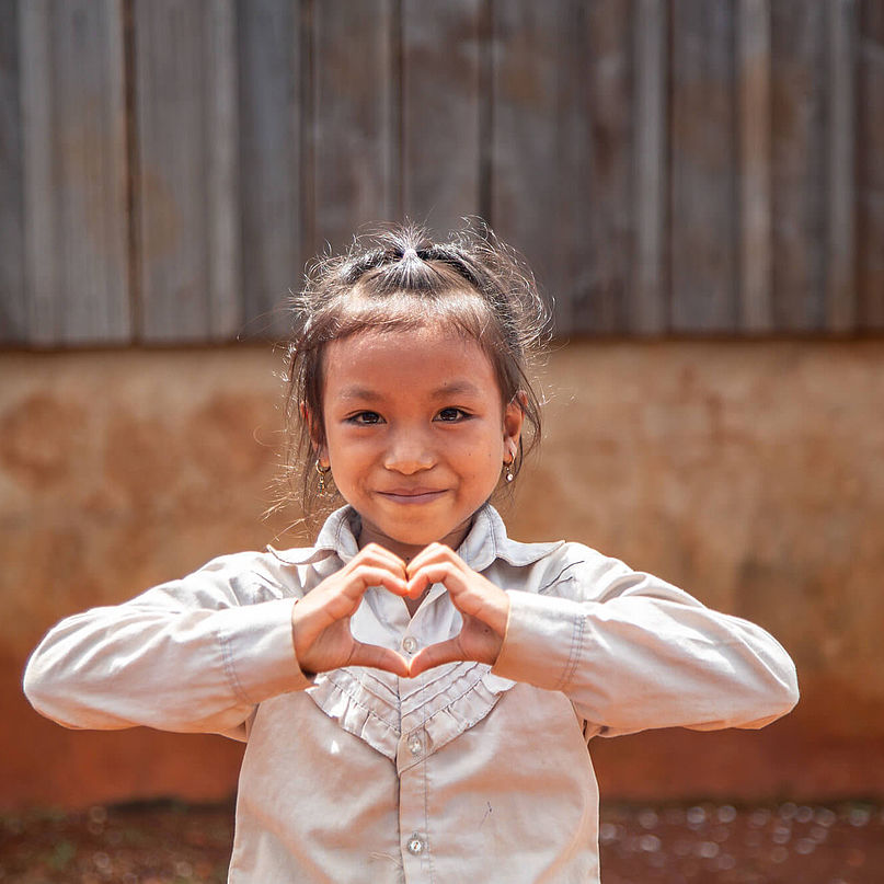 Ein Mädchen zeigt mit ihren Händen ein Herz, sie ist auf dem Weg zur Schule