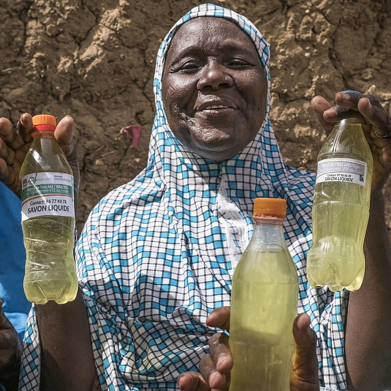Haoua Abdoulaye und ihre Nachbarinnen zeigen Flaschen mit selbsthergestellter Seife.