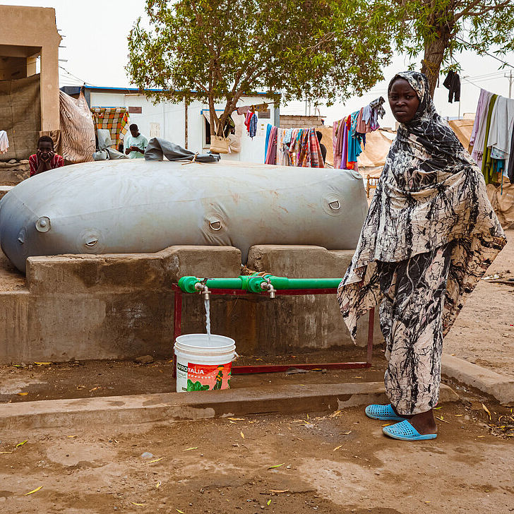 Frau steht vor einer Wasserblase von CARE und holt Wasser