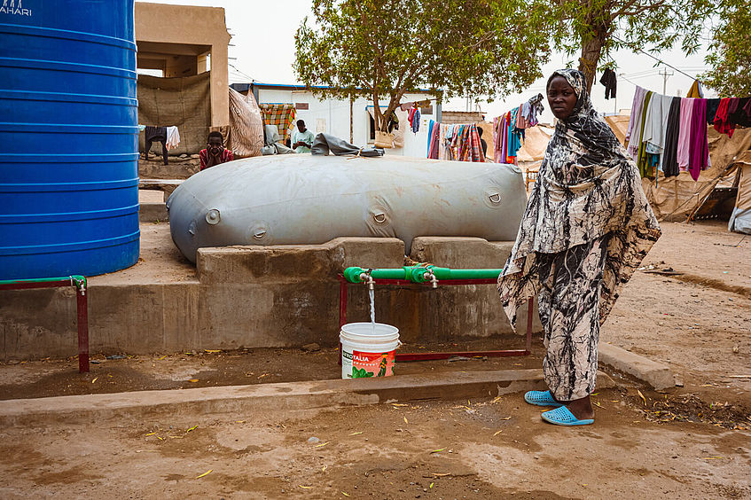 Frau steht vor einer Wasserblase von CARE und holt Wasser