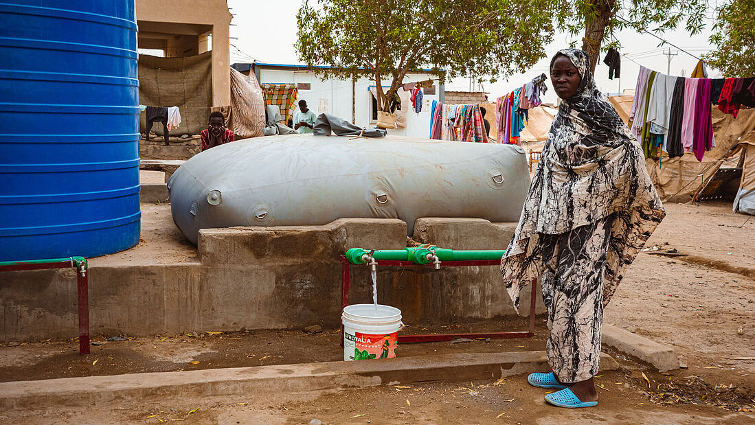 Frau steht vor einer Wasserblase von CARE und holt Wasser