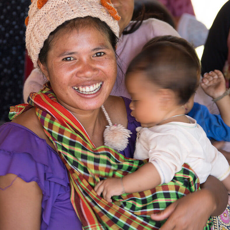 Eine Frau hält ihr Baby auf dem Arm und lacht in die Kamera