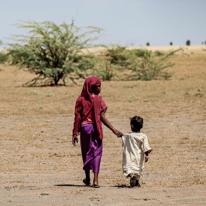 Zwei Kinder gehen Hand in Hand durch die Wüste