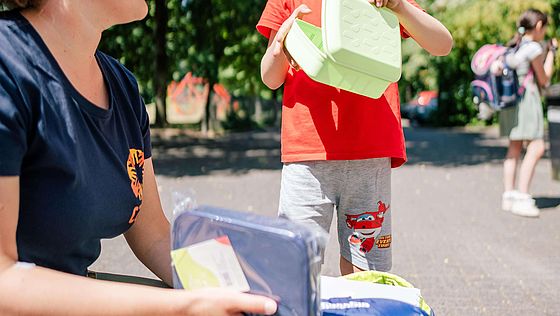 CARE-Mitarbeiterin verschenkt Schulranzen an kleinen Jungen im Rahmen des CARE-Schulstarter-Paket Projekts.