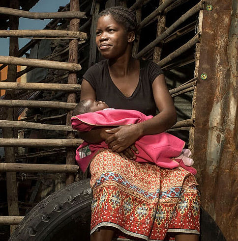 Manuela aus Mosambik sitzt auf einem großen Reifen und hält ihr Baby im Arm