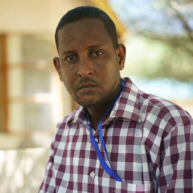 Der Aktivist Abdi Aden Bille im Flüchtlingscamp Dadaab in Kenia trägt ein kariertes Hemd und blickt ernst in die Kamera.