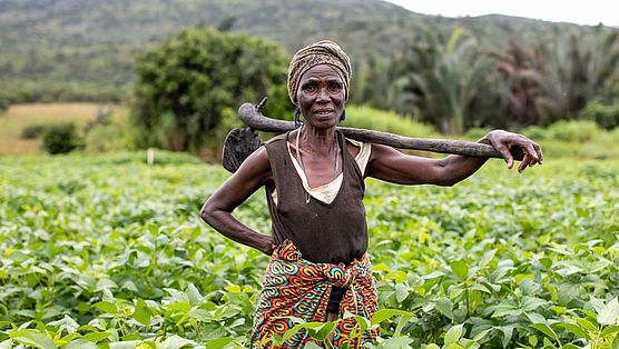 Bäuerin Mary steht mit einer Hacke über der Schulter auf ihrem Feld in Sambia.
