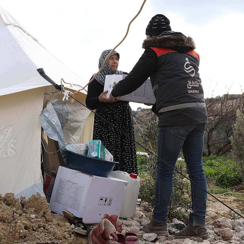 Ein Helfer von einer CARE Partnerorganisation in Syrien reicht einer Frau, die vom Erdbeben betroffen ist, ein CARE-Paket.